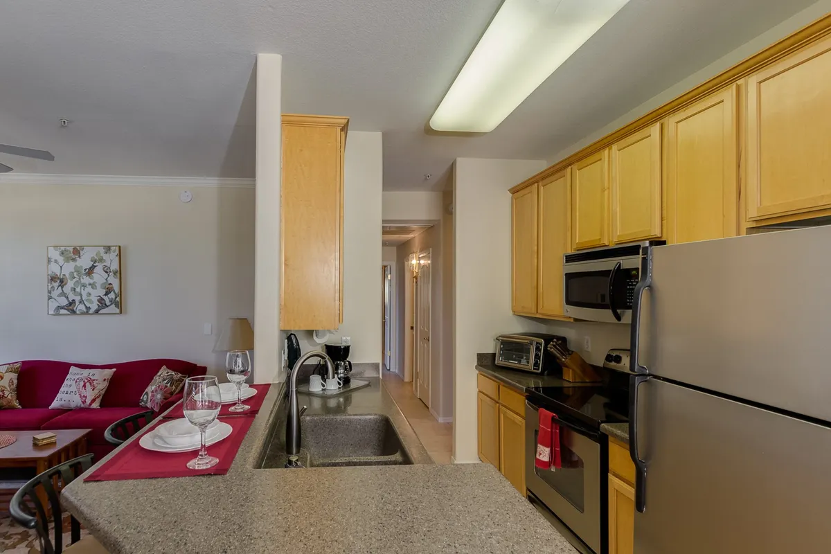 The image covers an open-plan view including the kitchen island, red sofa, kitchen appliances, and a dining area set for a meal. The composition showcases the seamless flow between the living and dining spaces, with warm lighting enhancing the atmosphere.