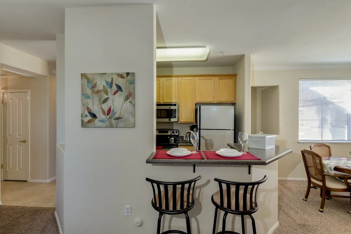 This scene focuses on a cozy breakfast bar with stools, adjacent to a view of kitchen appliances and a dining area beyond. The layout is ideal for sharing casual meals, morning coffee, or entertaining guests while cooking.