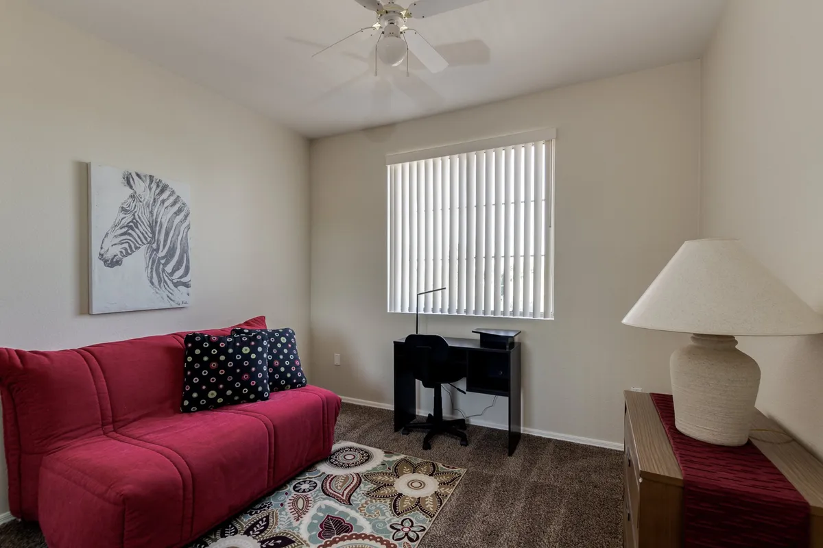 A flexible interior space with a desk and chair, colorful rug, lamp, and a red couch accented by zebra artwork, suitable for both work and relaxation.