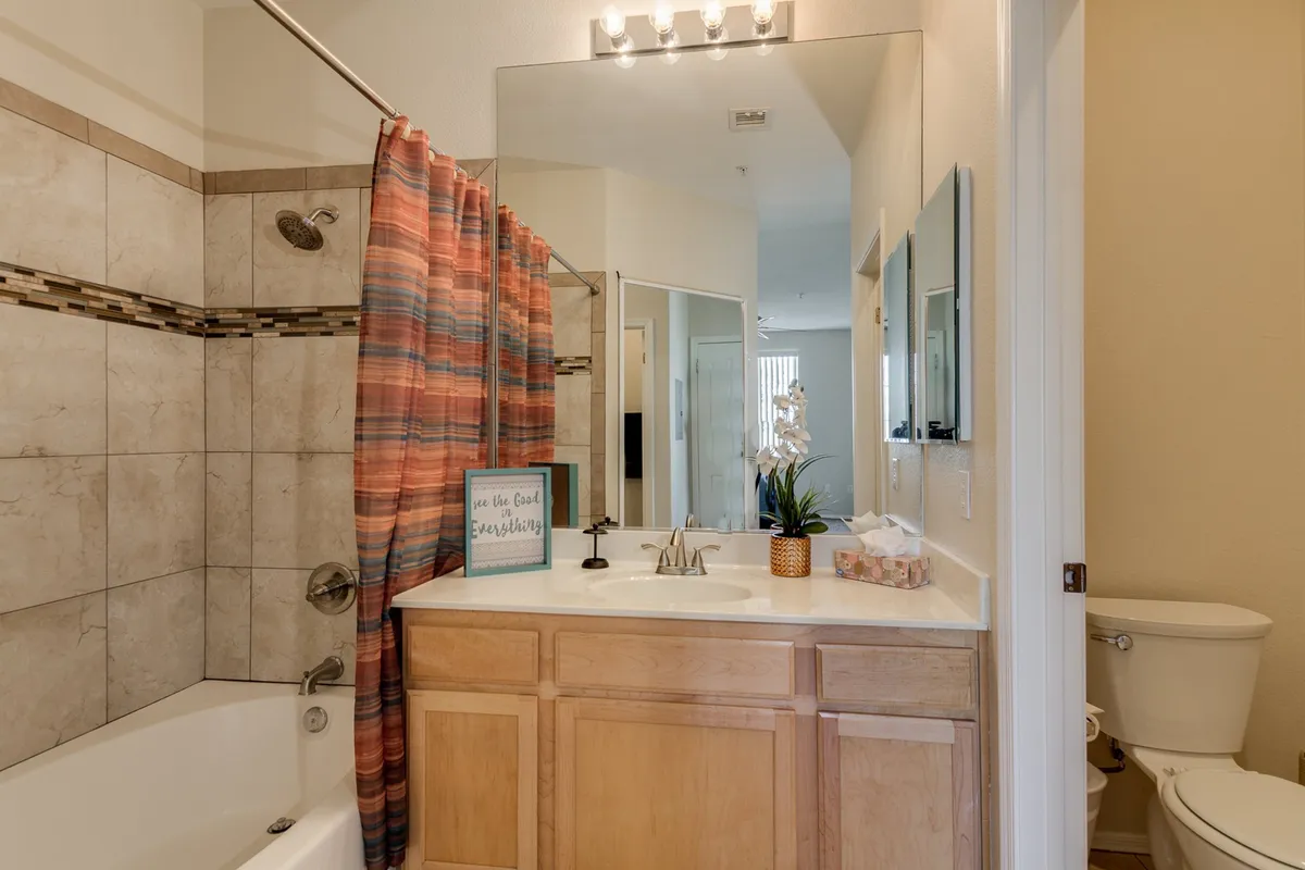 A calming bathroom with a bathtub, sink, mirror, and decorative sign. The light colors and spa-like setting invite relaxation and self-care.