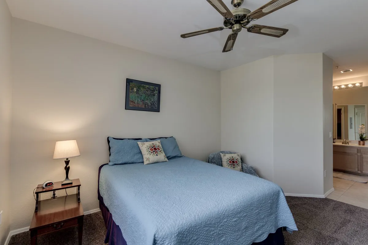 A tranquil bedroom scene featuring a bed with a blue quilt, a nightstand with a lamp, and framed artwork above the bed. Soft lighting creates a peaceful, inviting atmosphere ideal for unwinding.