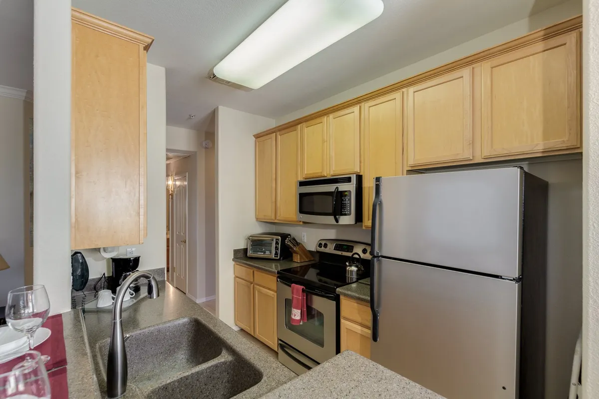 A welcoming kitchen interior featuring stainless steel appliances, granite countertops, and warm wooden cabinets. The space is arranged for both cooking and casual gatherings, with a cozy, functional mood.