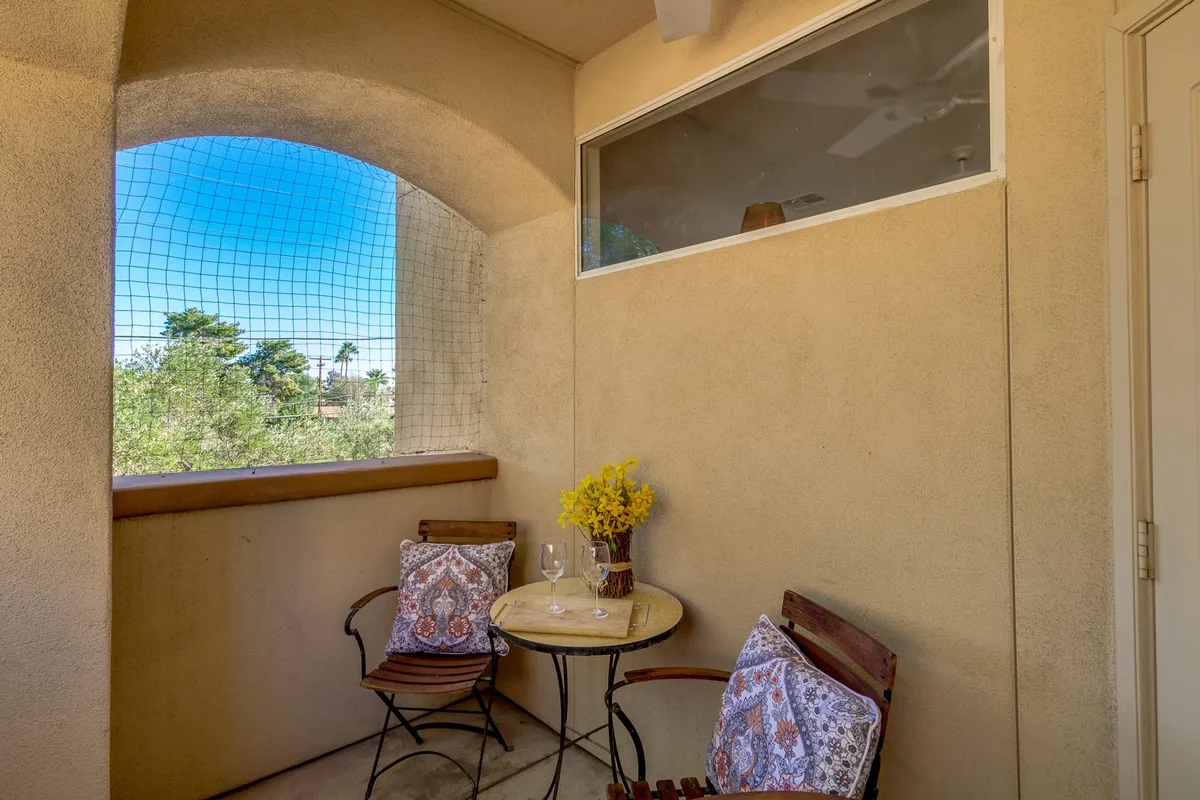 A small round table with two chairs sits near a window, with a vase of fresh flowers and two glasses on the tabletop. Soft daylight filters in, creating a cozy, inviting nook, ideal for morning coffee or a quiet conversation. The setting hints at a private retreat connected to the outside world.
